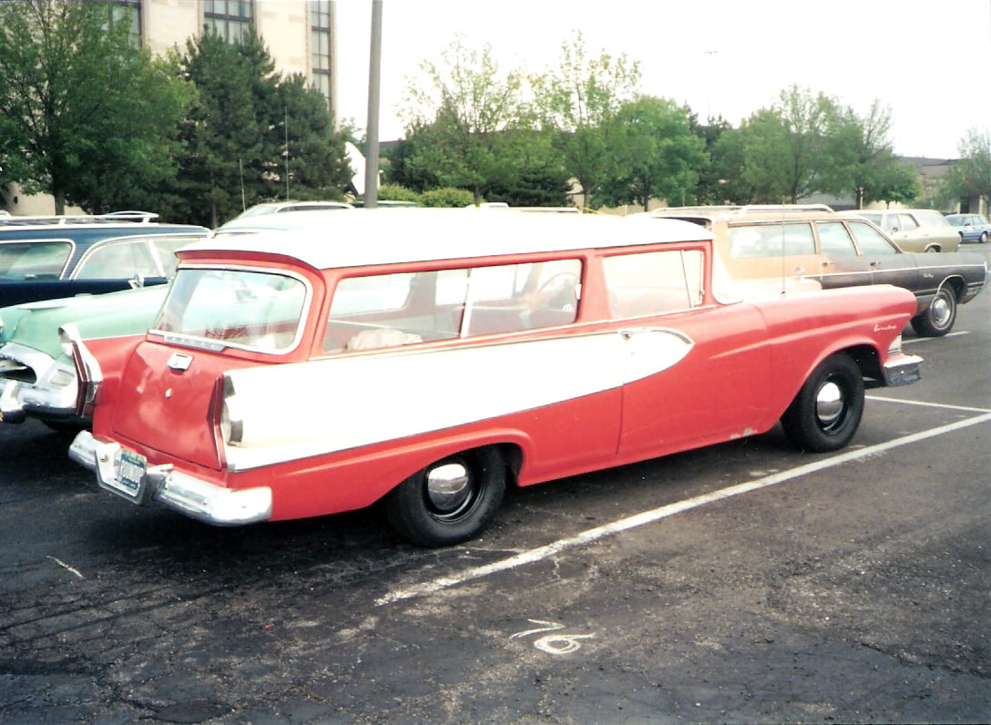 A red and white vintage station wagon parked in a parking lot.