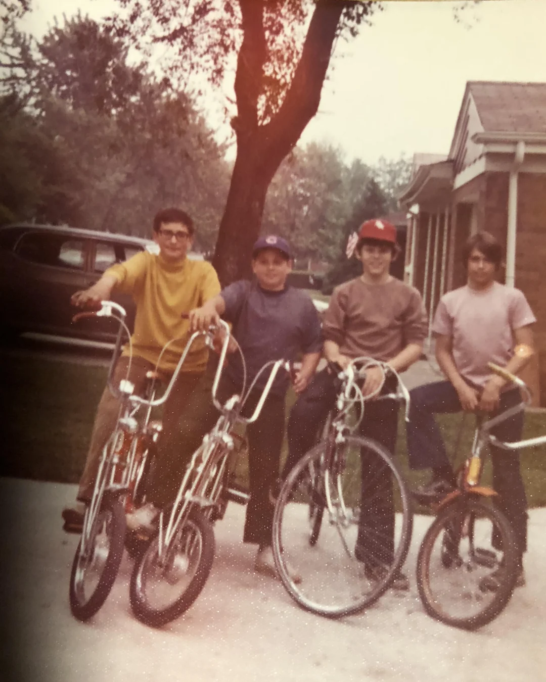 Four teenage boys standing in a driveway with their bicycles.
