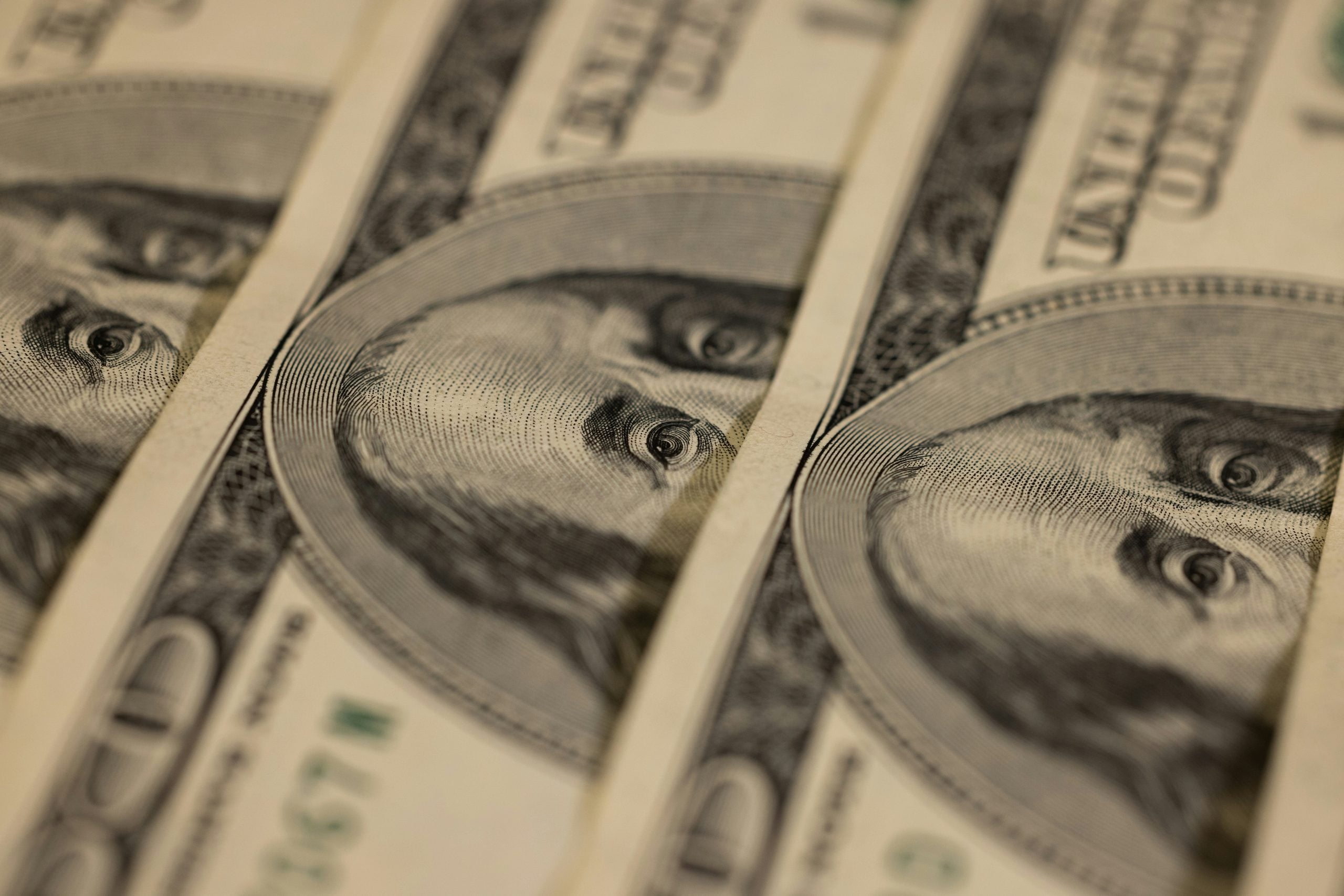 Close-up view of several stacked one hundred dollar bills showing the portrait of Benjamin Franklin.