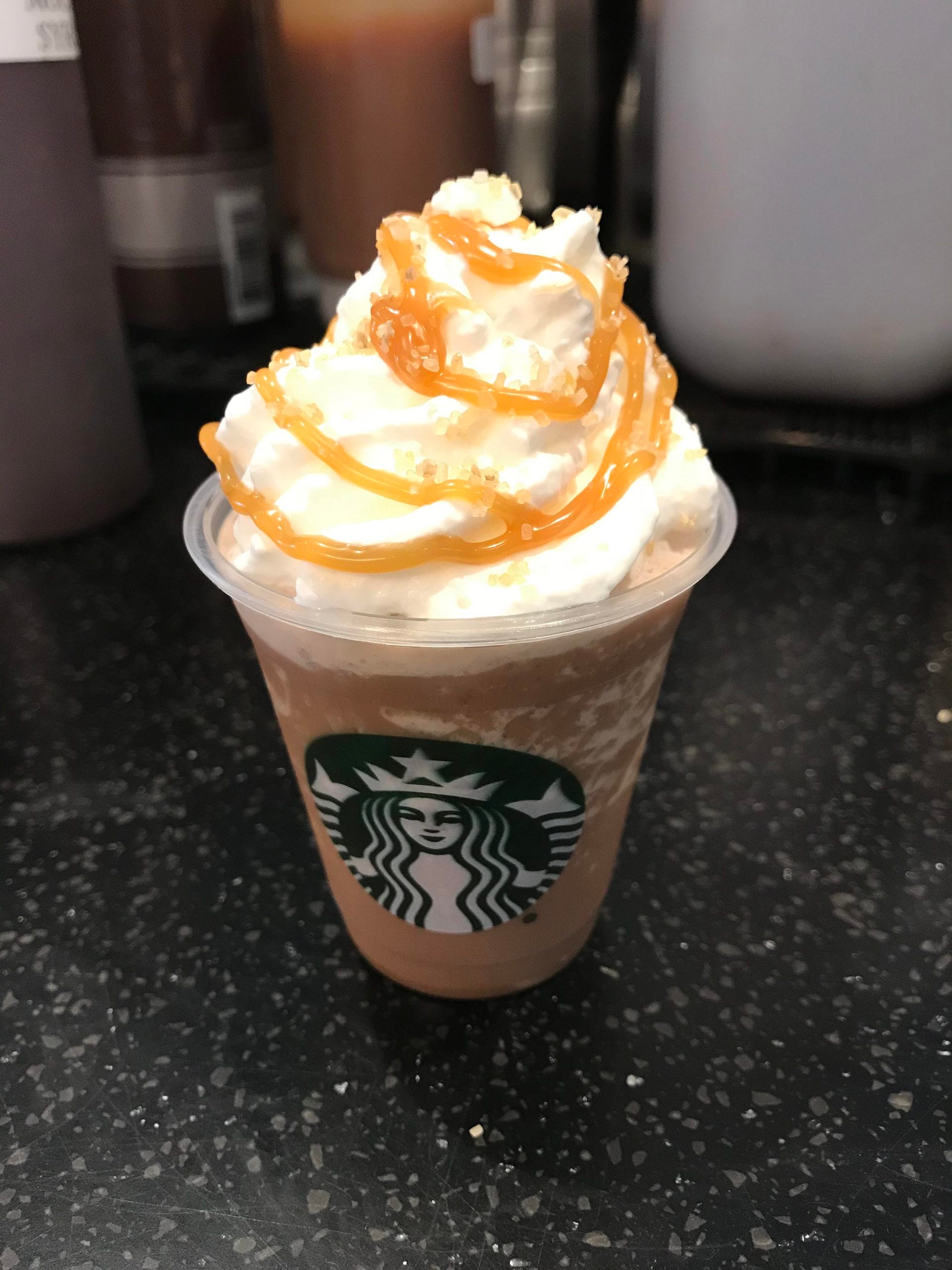 A Starbucks Frappuccino topped with whipped cream, caramel drizzle, and brown sugar sprinkles.