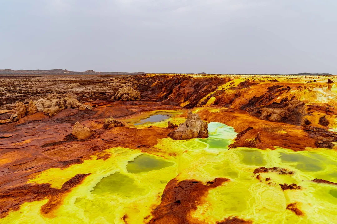 Bright yellow and rust-colored mineral formations surround small, vibrant green pools in the Dallol hydrothermal field.