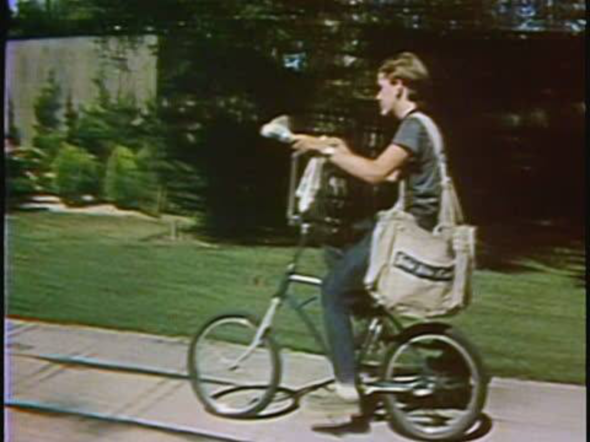 A person riding a bicycle with a large canvas bag slung over their shoulder.