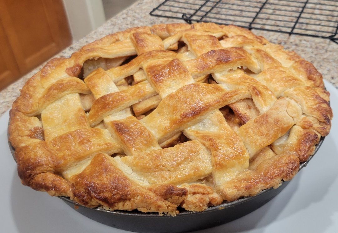 A baked apple pie with a golden-brown lattice crust in a pie dish.