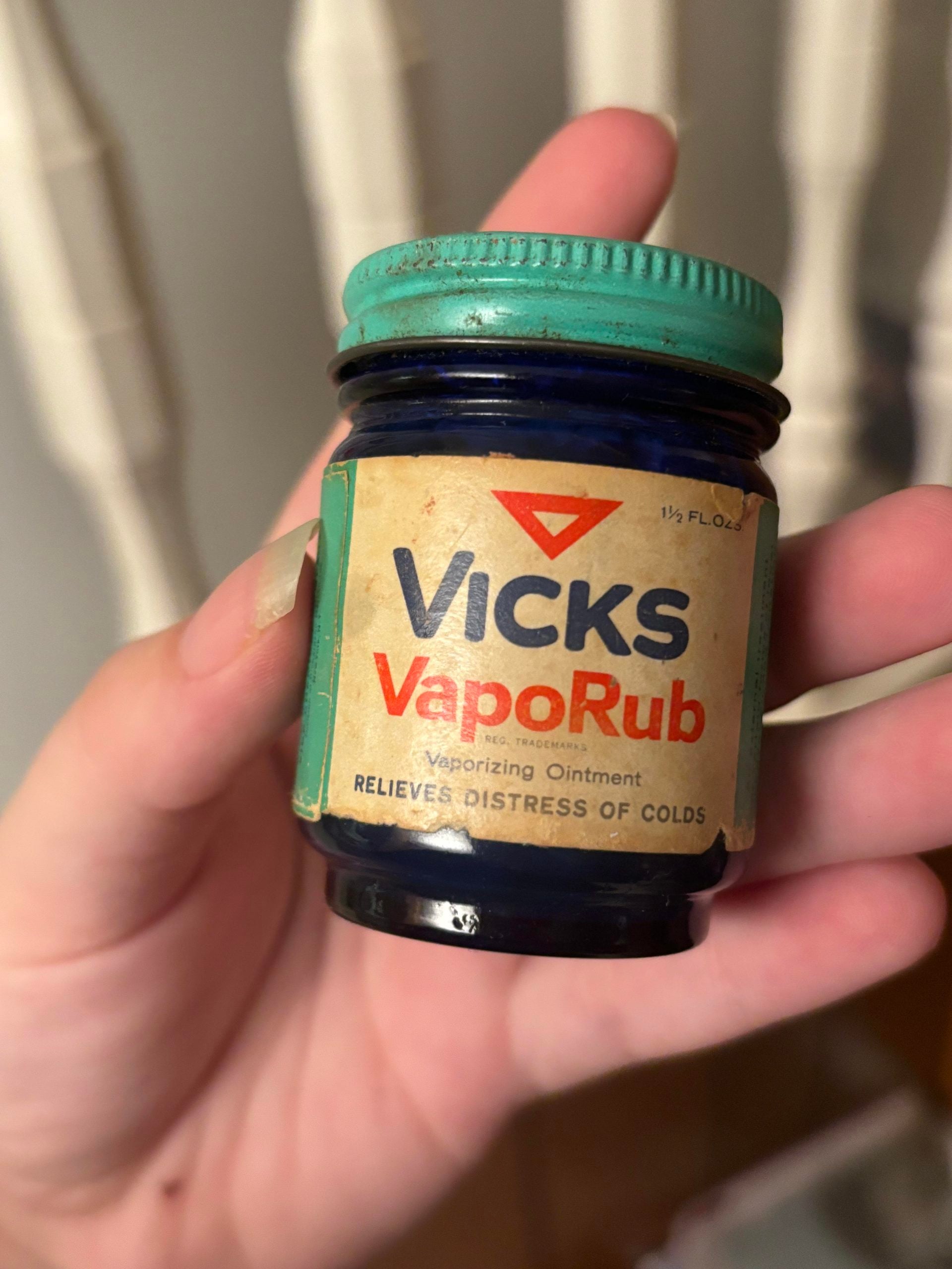 Hand holding a small, vintage blue glass jar of Vicks VapoRub with a teal metal lid.