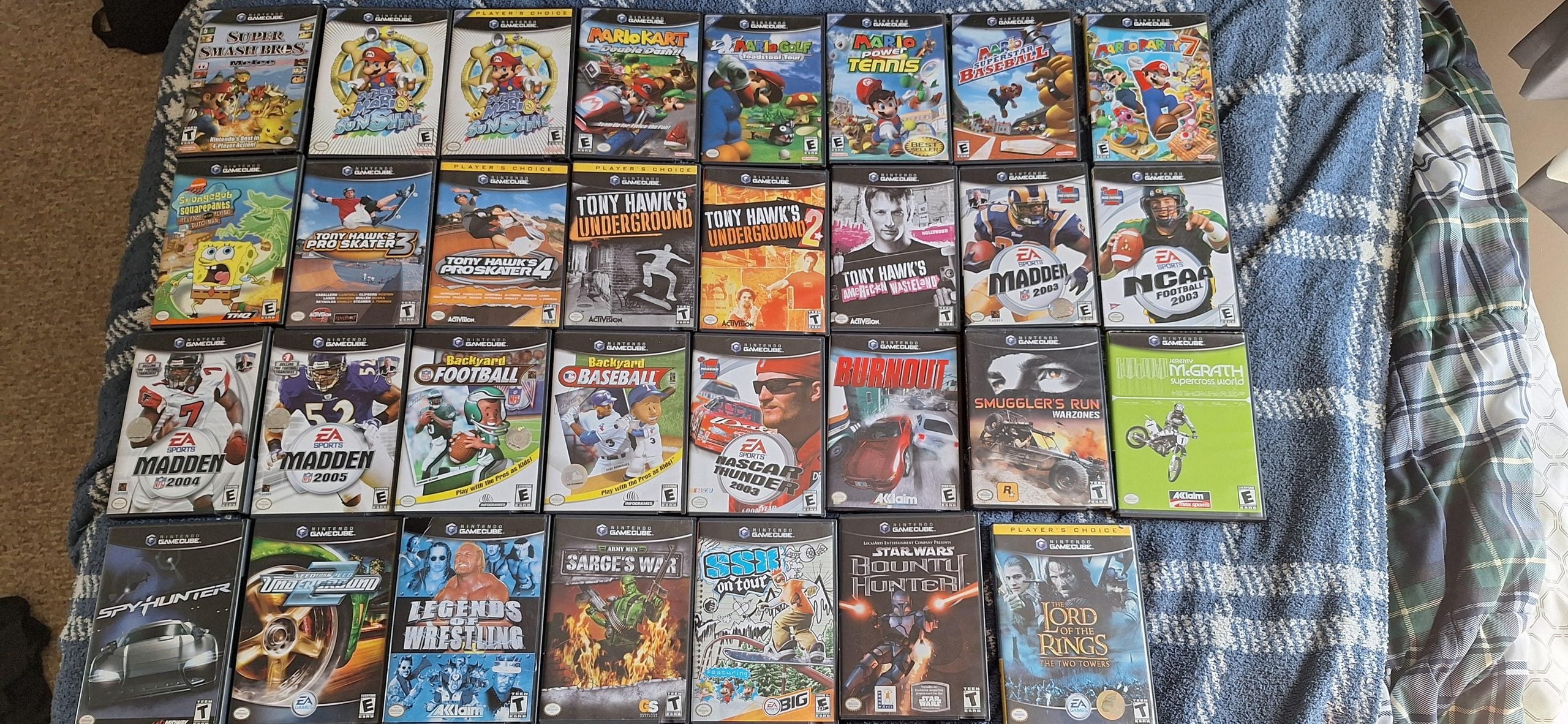 A collection of twenty-nine Nintendo GameCube video games arranged in a grid on a blue plaid blanket.