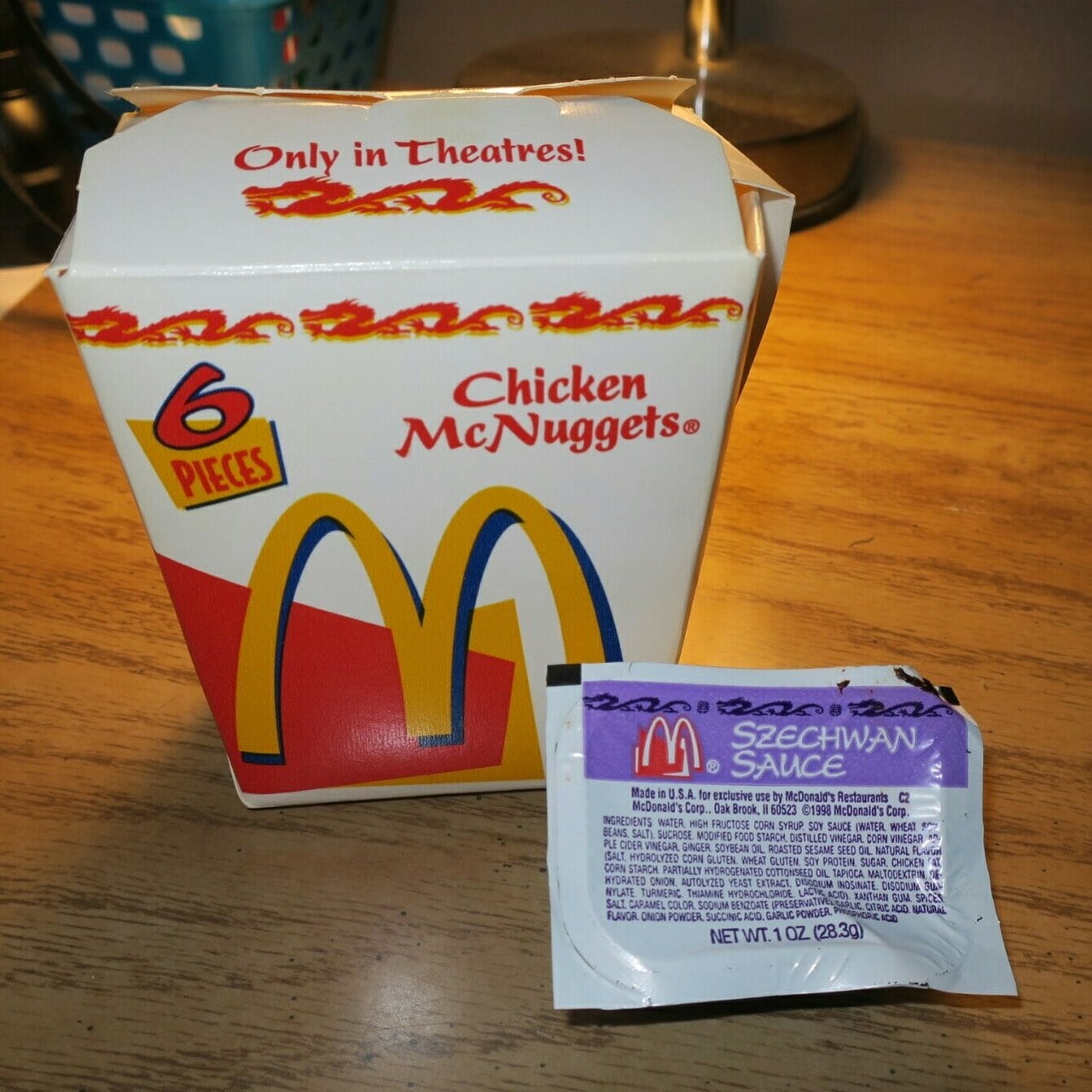 A McDonald’s 6-piece Chicken McNuggets box and a packet of Szechuan Sauce on a wooden table.