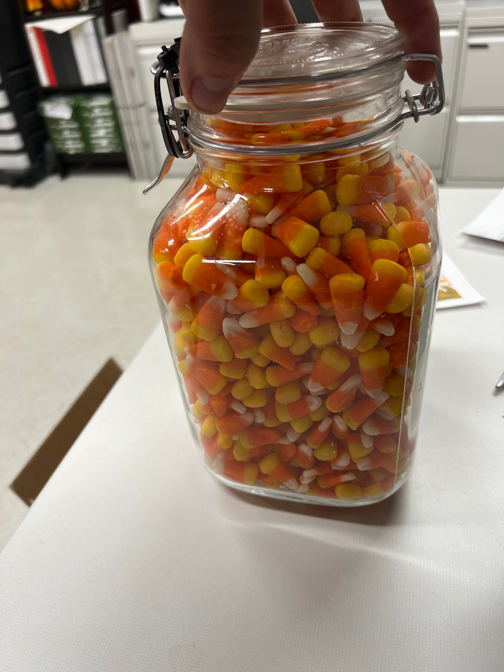 A hand holding the lid of a glass jar filled with candy corn.