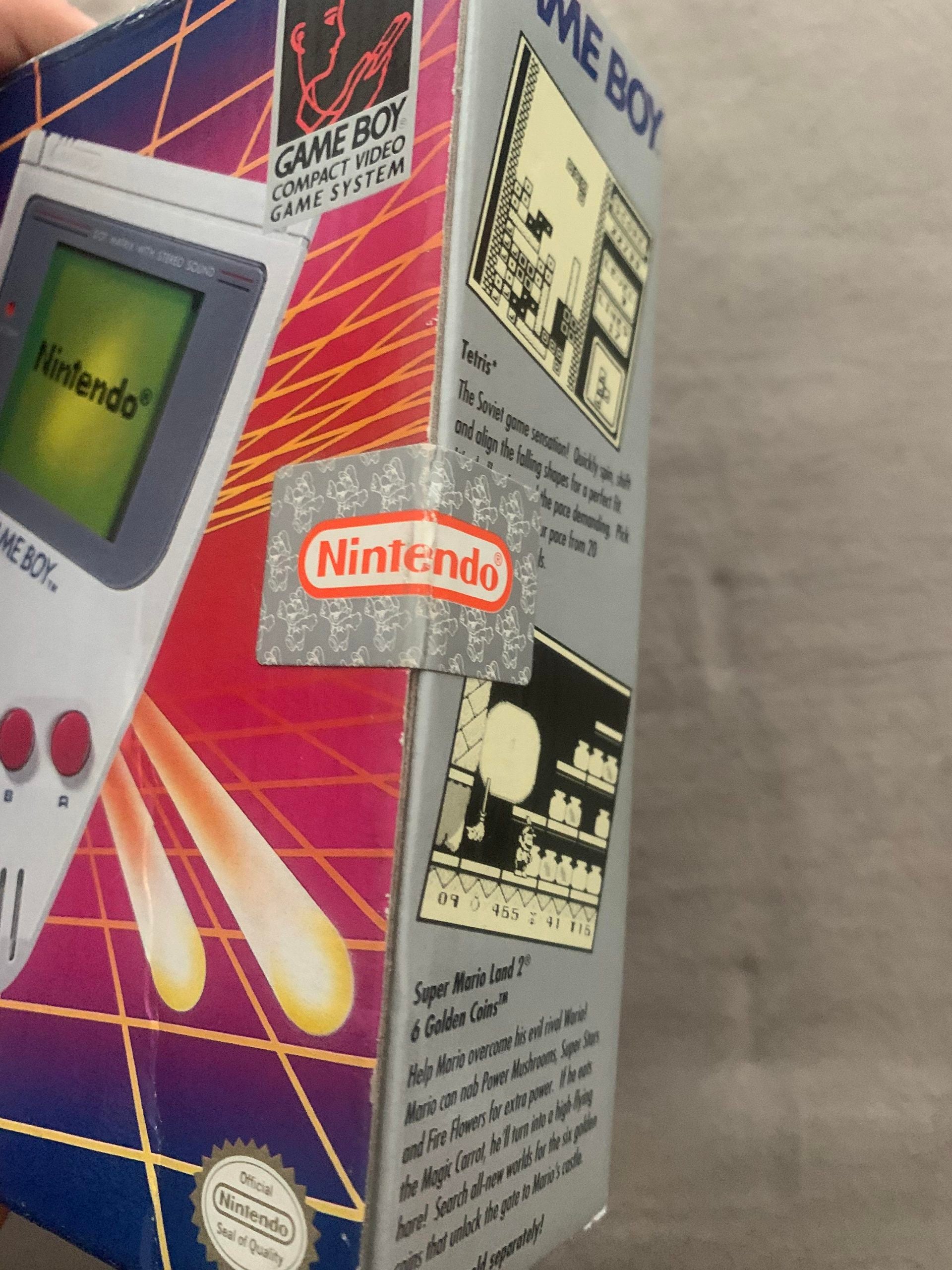 Close-up of a Game Boy box showing the Nintendo logo seal, part of the console, and info about Tetris and Super Mario Land with black and white game screenshots.