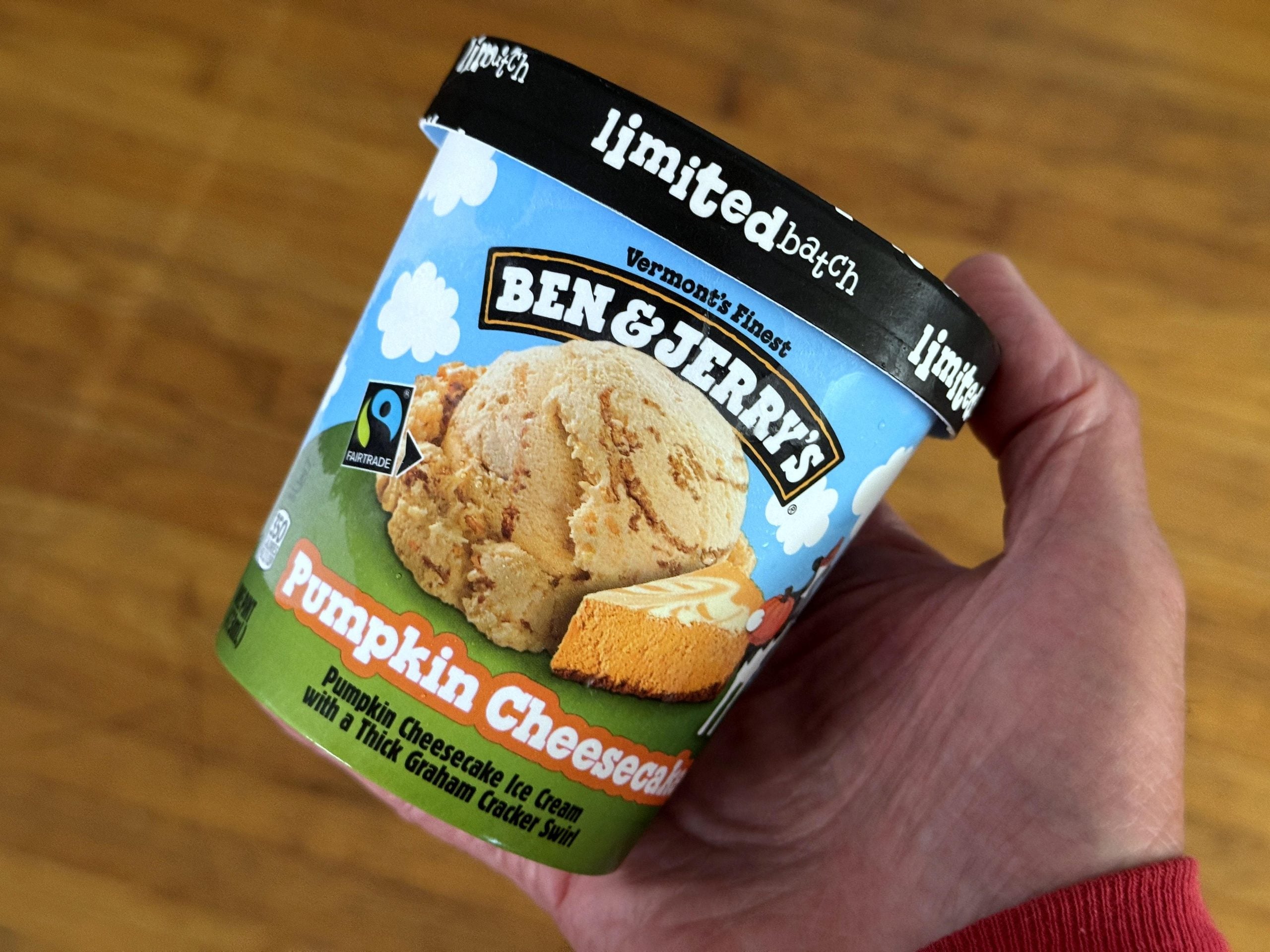 A hand holds a pint of Ben & Jerry’s Pumpkin Cheesecake ice cream.