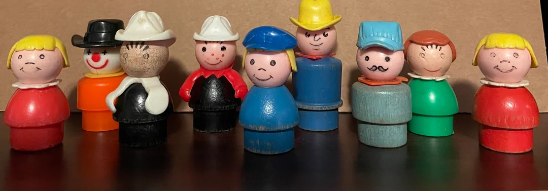 Nine vintage Fisher-Price Little People figurines are lined up, each with different painted outfits, hats, and facial expressions, standing on a dark surface with a brown background.