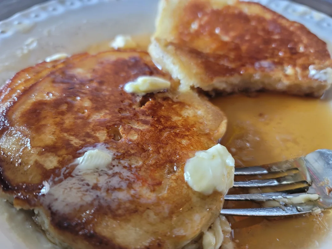 Close-up of pancakes with melting butter and syrup on a plate, with a fork resting next to a partially cut piece.