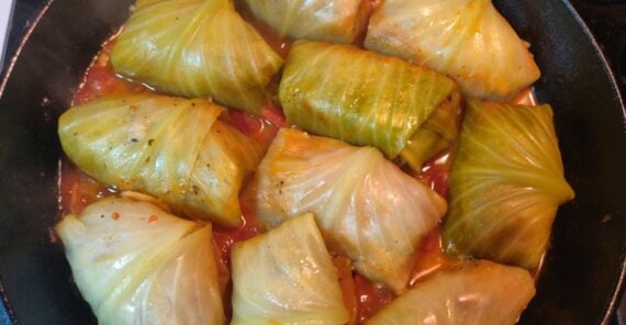 Cabbage rolls cooking in a skillet, tightly wrapped in cabbage leaves, simmering in a tomato-based sauce.