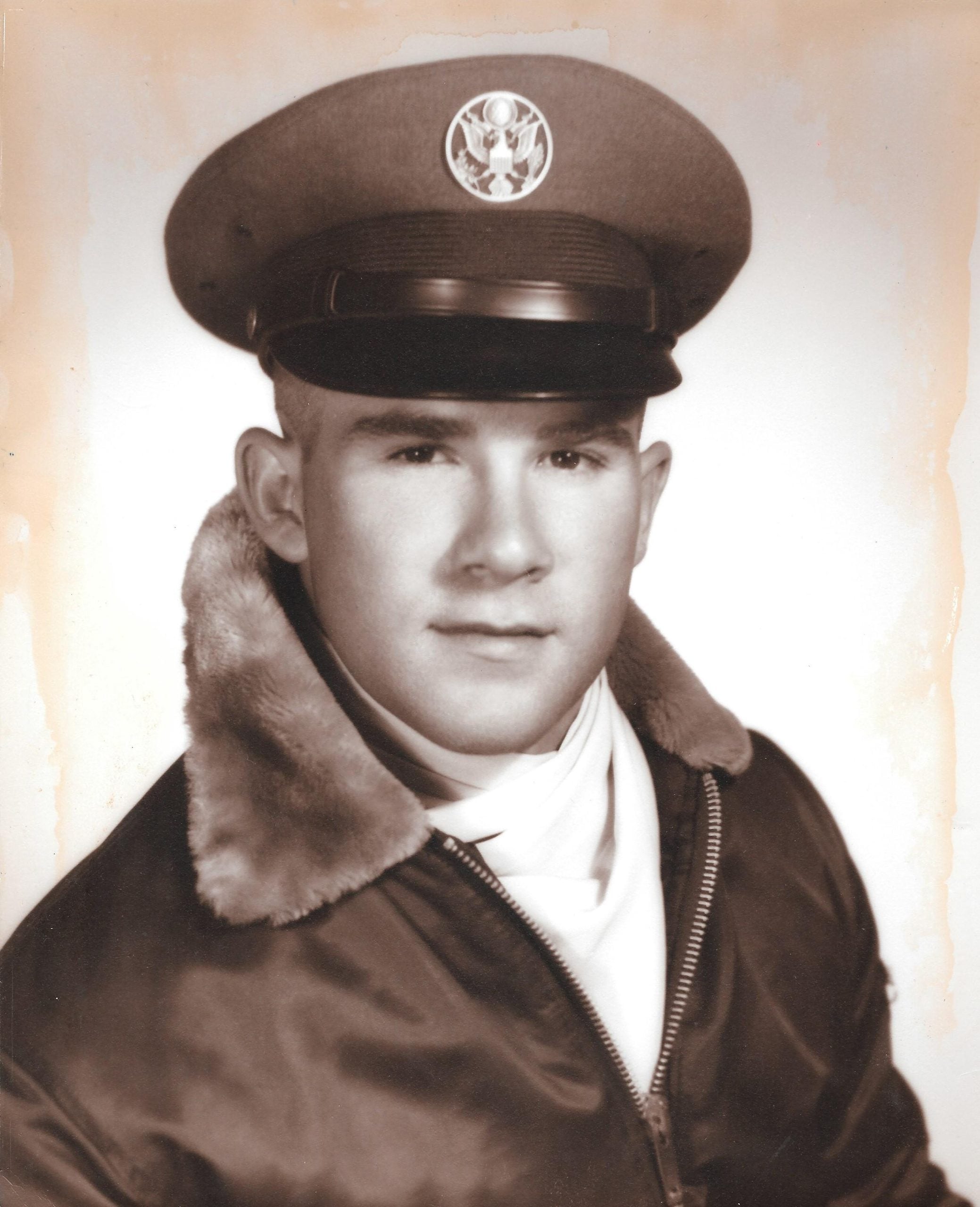 A sepia-toned portrait of a young man in a military uniform, wearing a flight cap with an insignia and a jacket with a fur-lined collar.