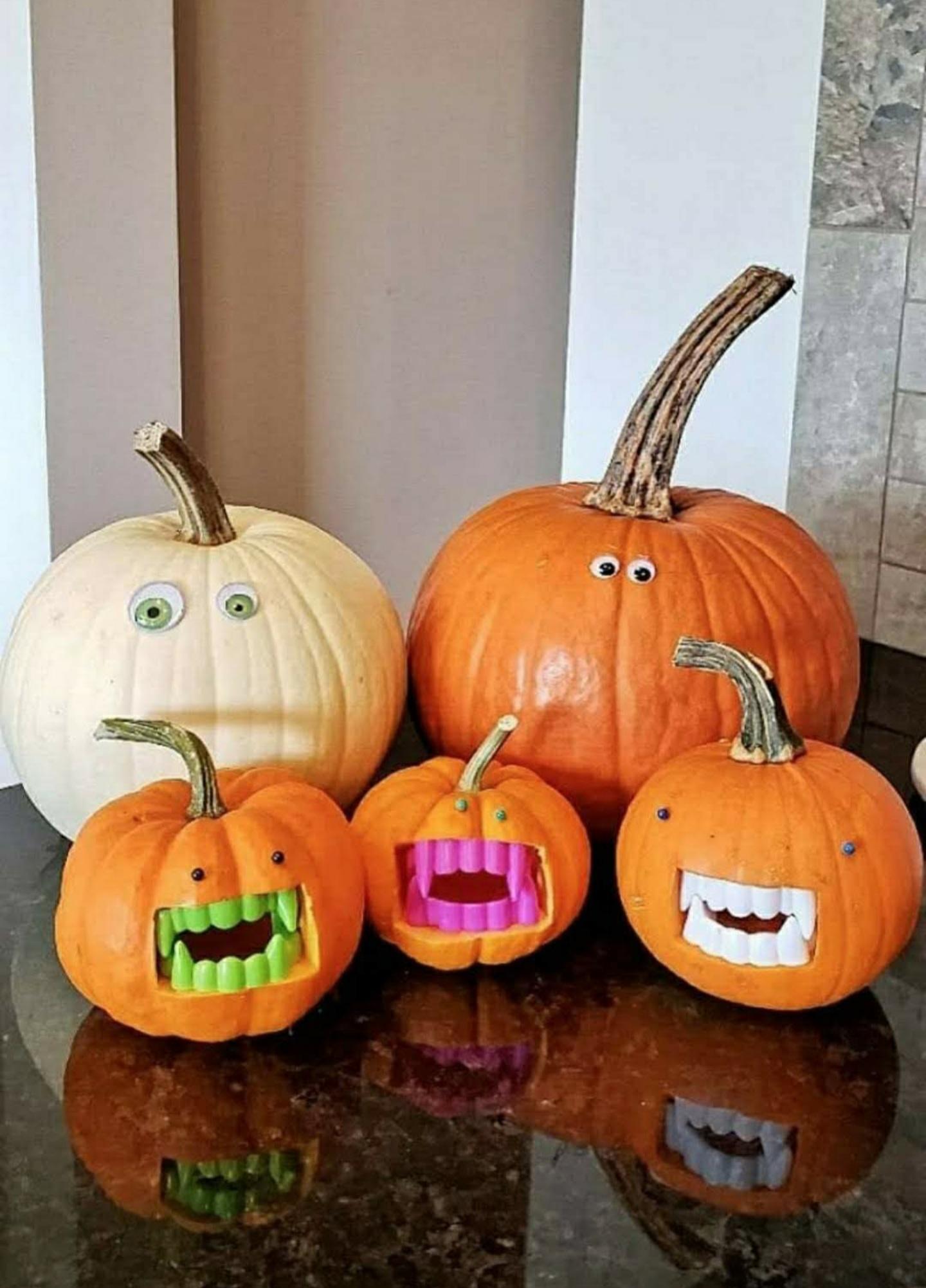 Five pumpkins decorated with googly eyes and plastic novelty teeth sitting on a dark surface.