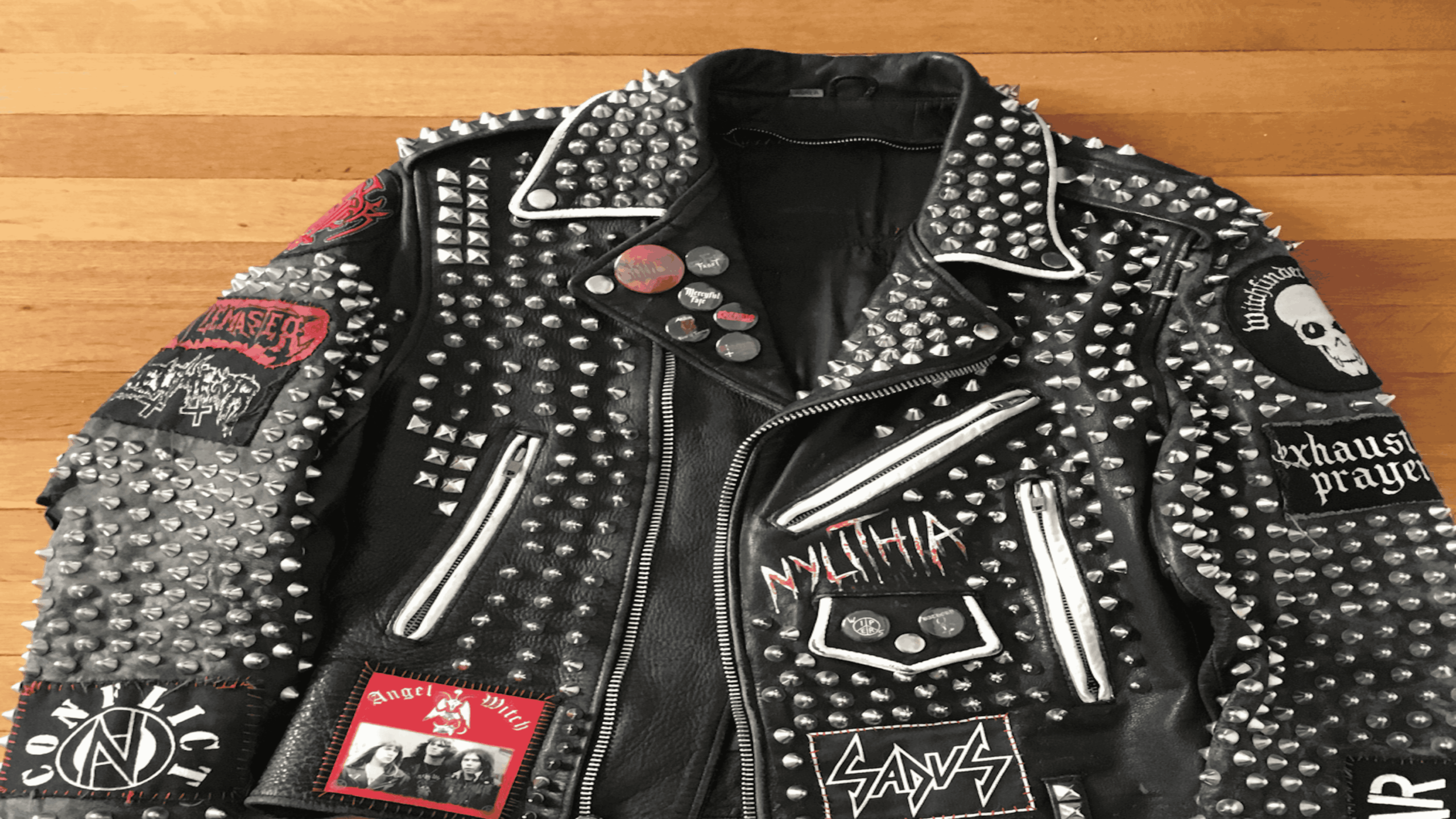 Black leather motorcycle jacket heavily decorated with metal studs and various band patches.