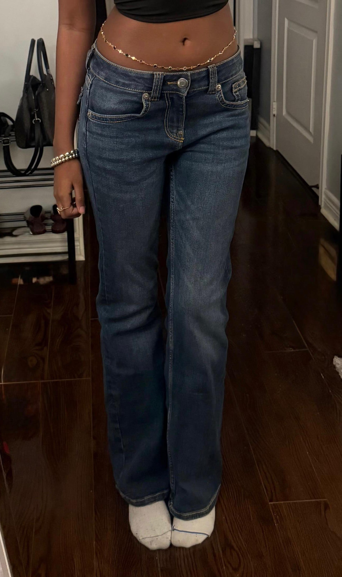 A person wearing a cropped top, low-rise blue jeans, and a delicate gold belly chain.