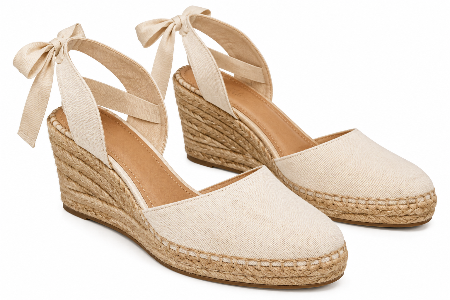 Pair of cream-colored canvas wedge espadrilles with ankle tie ribbons and braided jute midsoles.