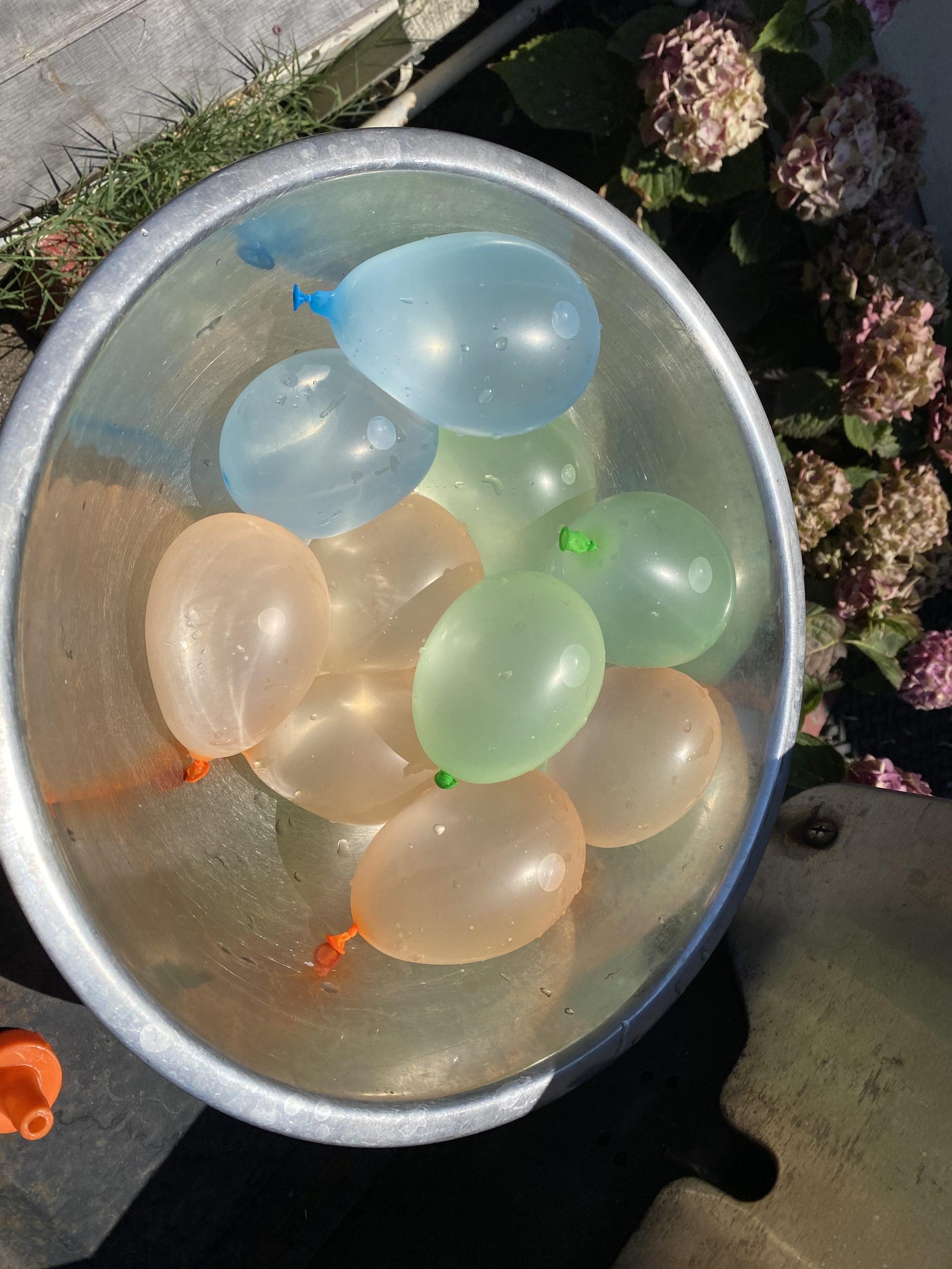 A metal bowl filled with blue, green, and orange water balloons.