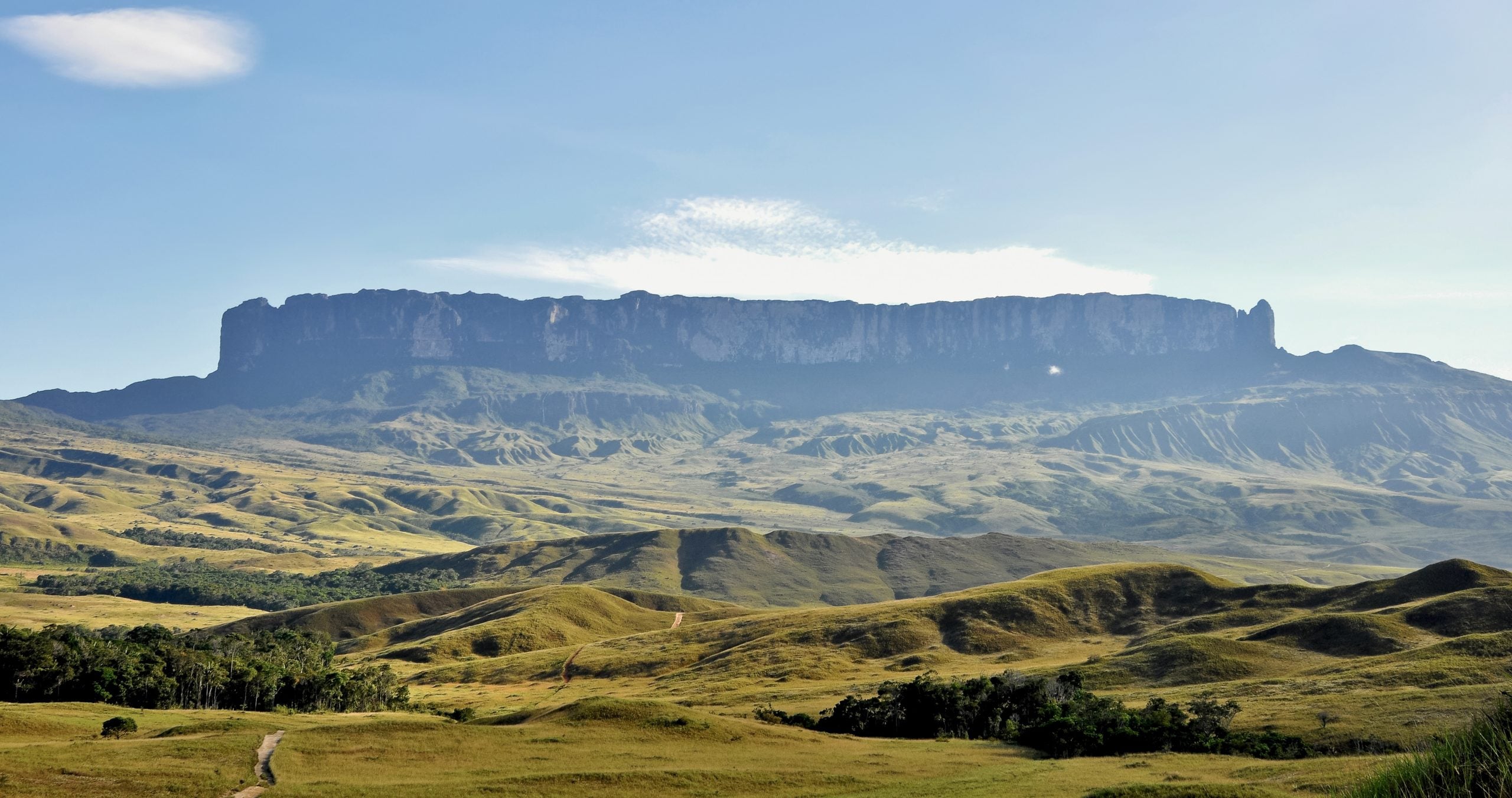 A flat-topped mountain rises above rolling, grassy hills under a clear blue sky.