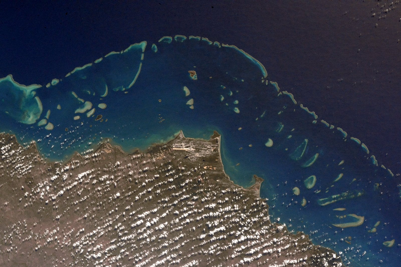 Satellite view of a coastal region bordering a coral reef and deep blue ocean.