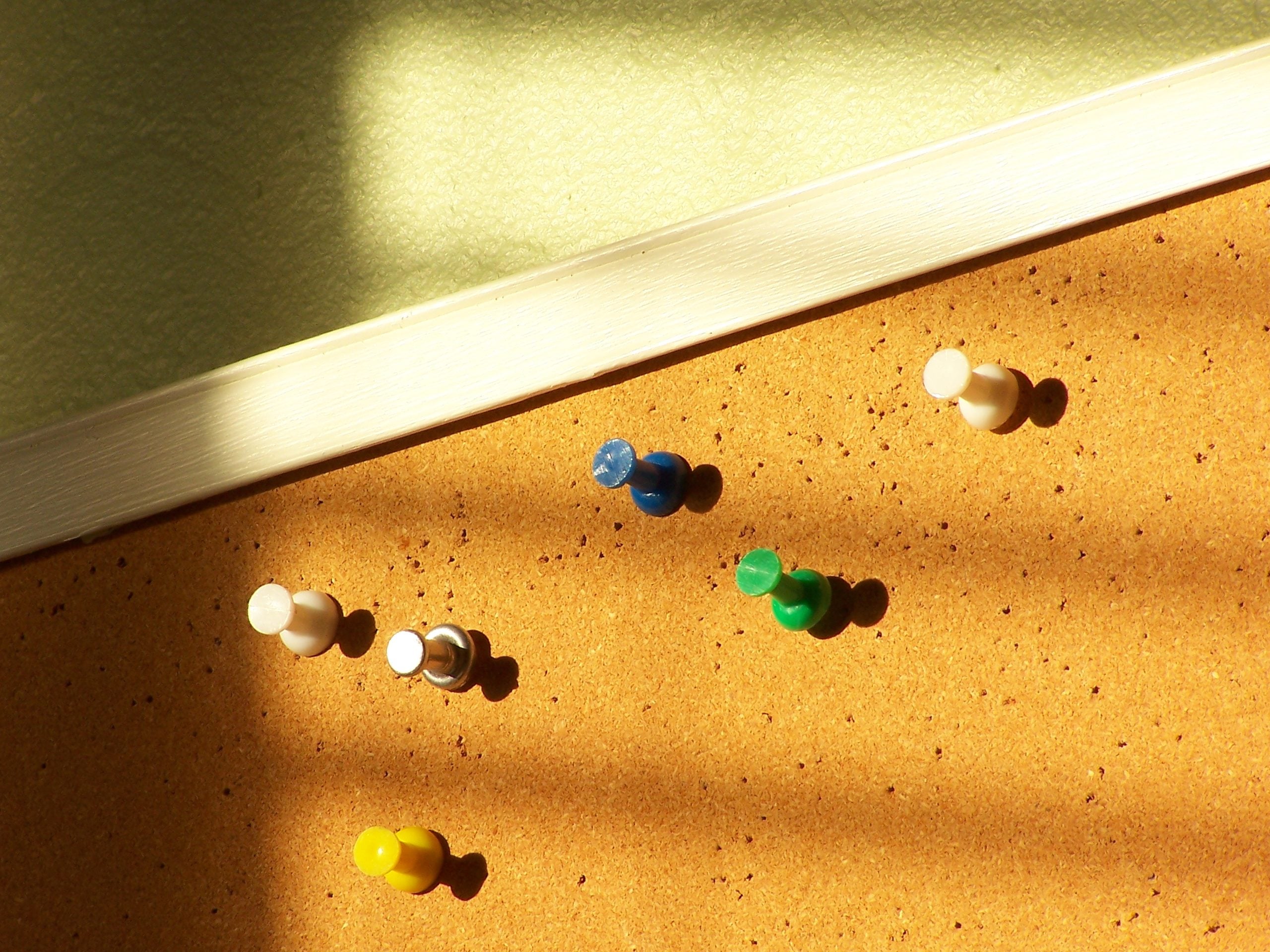 Six colorful plastic pushpins stuck into a cork bulletin board.