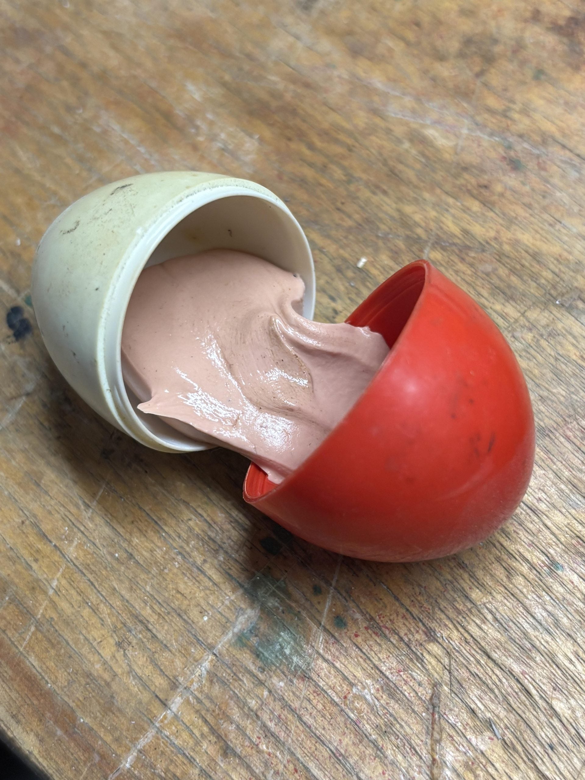 A half-open plastic egg container spilling out a pale pink, putty-like substance.