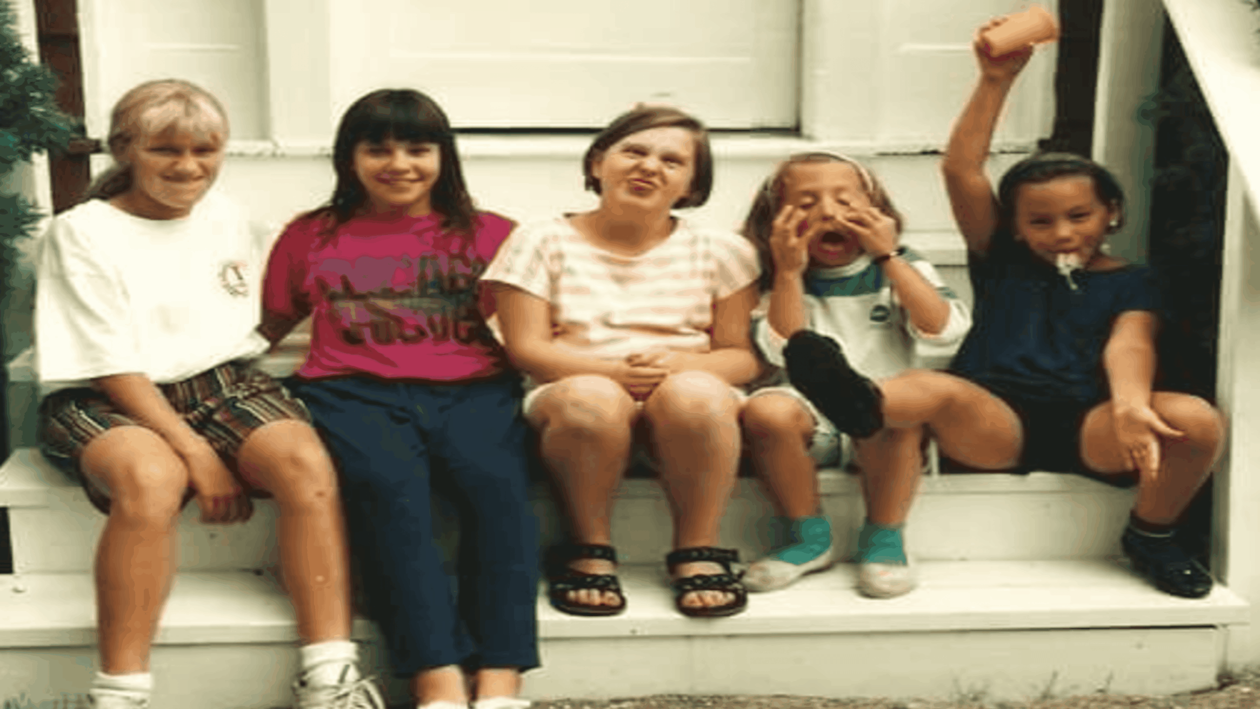 Five young girls sitting on white porch steps, with one girl raising a cup in the air.