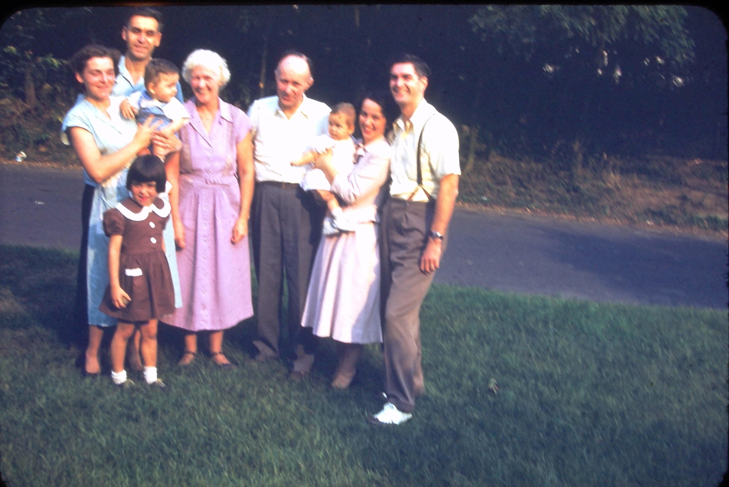 A family of eight posing for a portrait outdoors on a grassy lawn.
