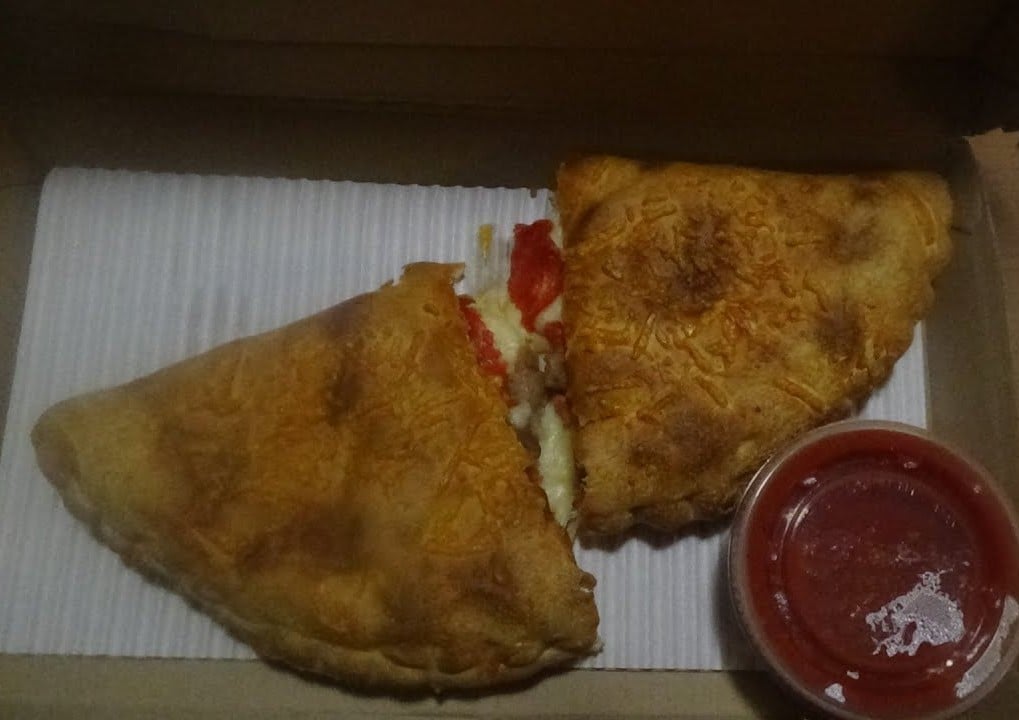 A calzone cut in half with visible cheese and red filling, served in a box with a side of marinara sauce.
