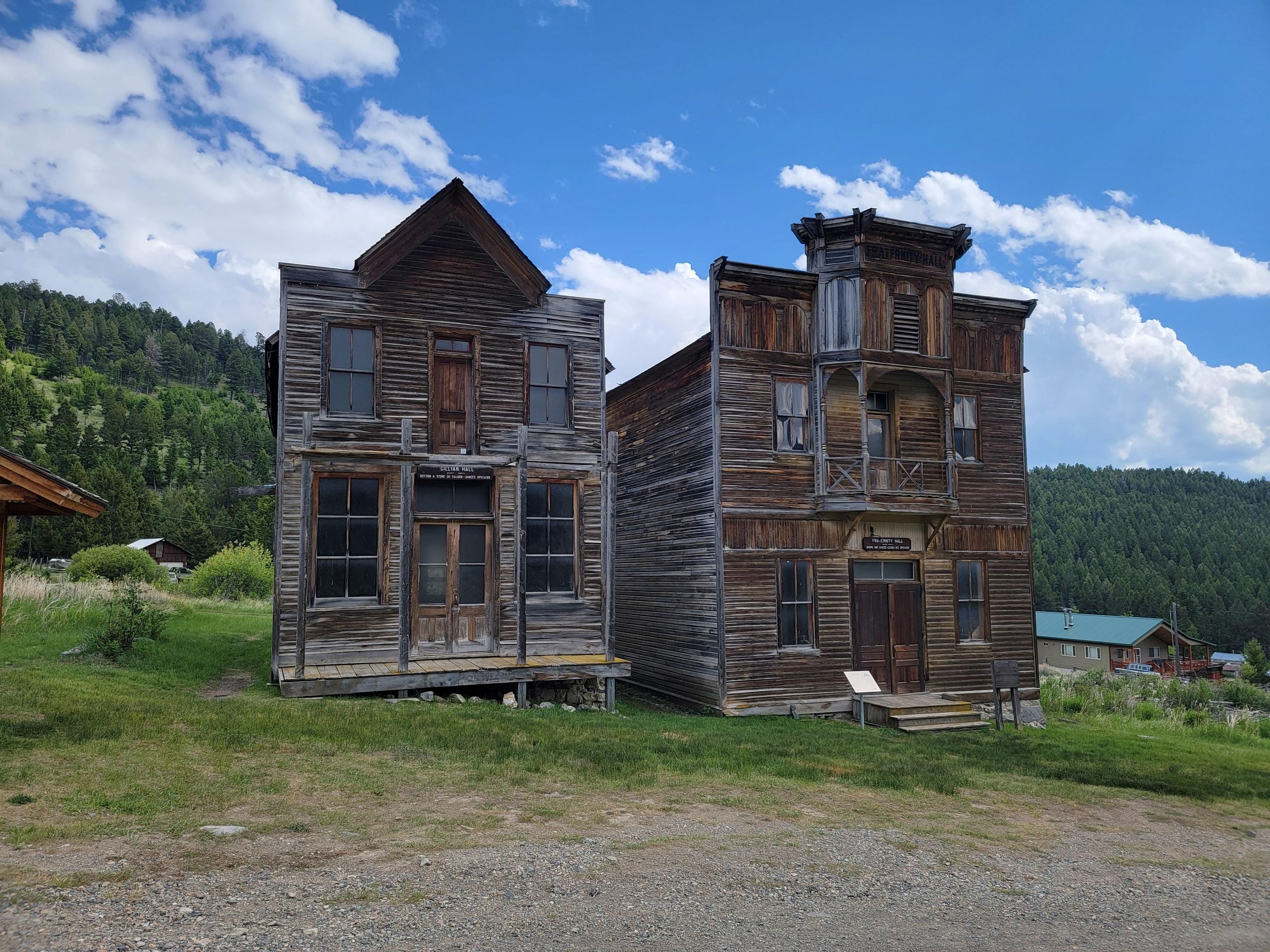 Two weathered, two-story wooden buildings in a mountain setting, identified by signs as Galtier Hall and the Odd Fellows Hall.