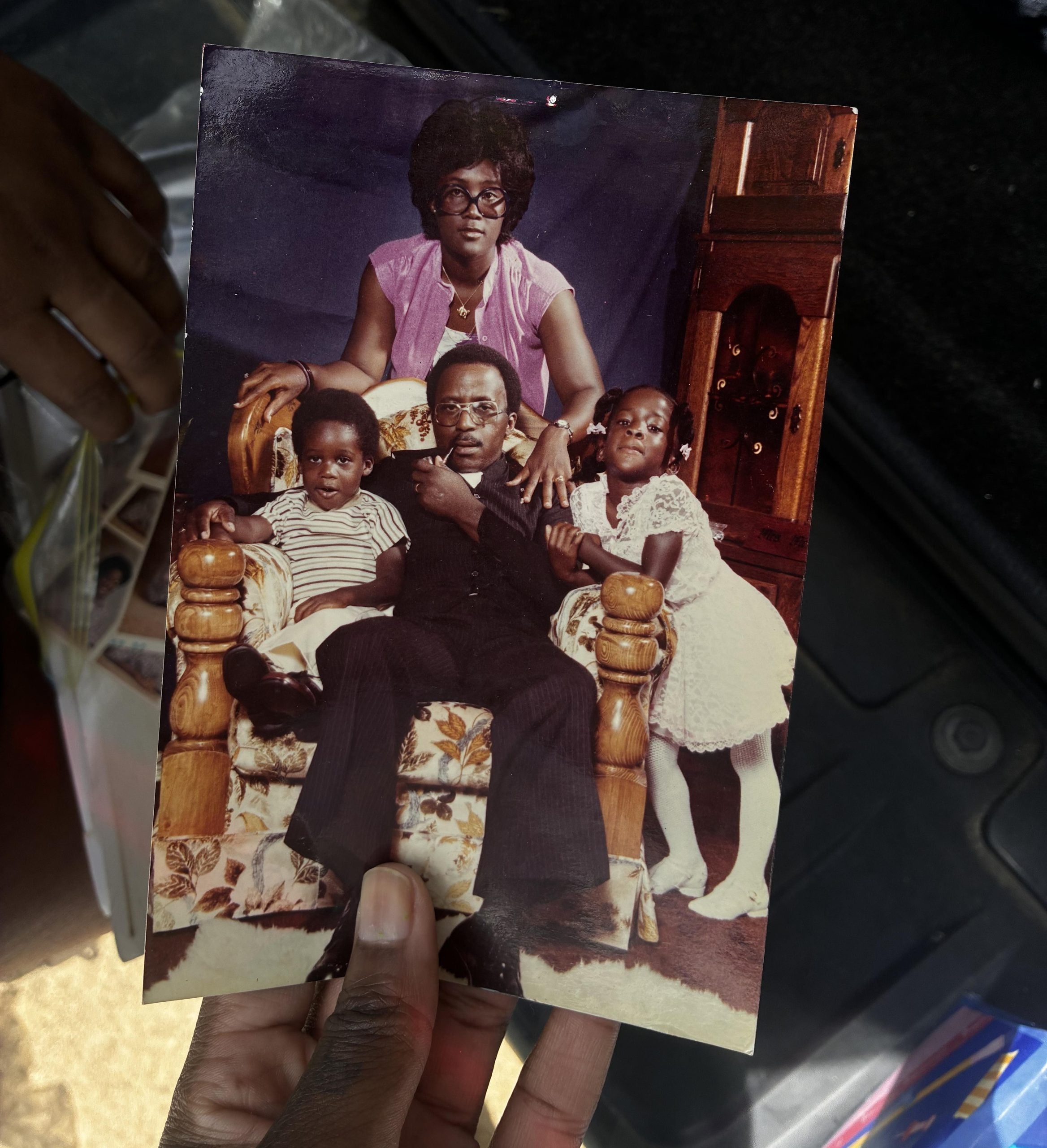 A vintage portrait of a family of four posing in a floral armchair, with a man seated in the center, a woman standing behind him, and two young children beside them.