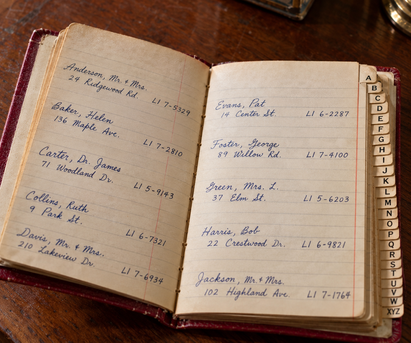 An open address book with handwritten names, addresses, and phone numbers organized alphabetically by tabbed pages.