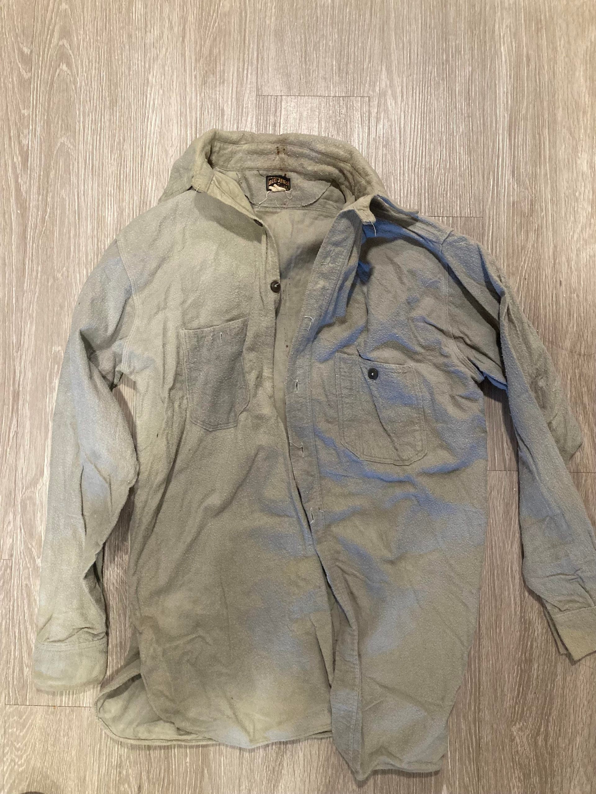 A light gray long-sleeve button-up shirt with two chest pockets lies spread out on a wood-patterned floor.