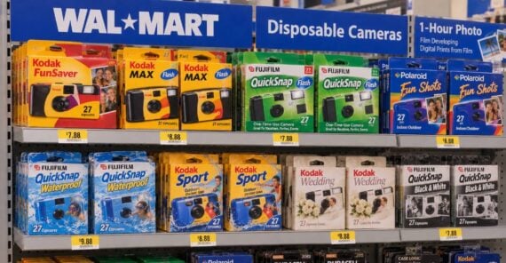 A retail shelf at Walmart stocked with various disposable cameras, film rolls, and camera batteries, each with a price tag displayed below.