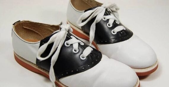 A pair of black and white saddle shoes with white laces and red soles.