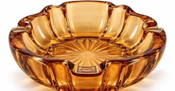 A round, amber-colored glass ashtray with scalloped edges and a sunburst pattern on the base.