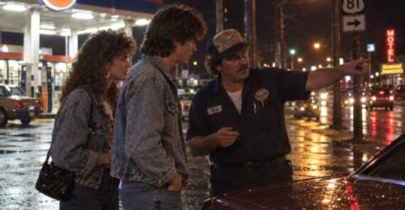 A Gulf gas station attendant in a uniform points toward the road for a young couple standing beside a car at night.