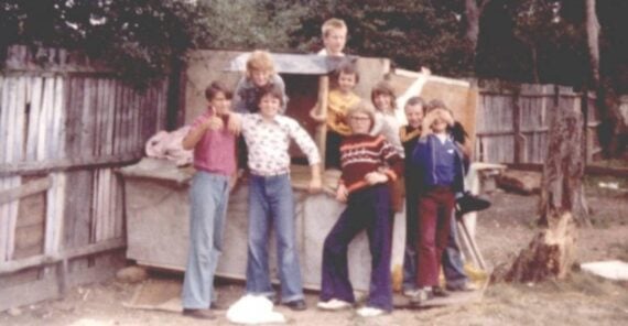 A group of seven children standing in and around a wooden play structure in a yard.