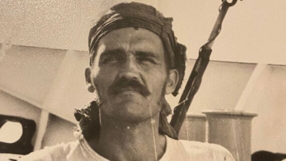 Sepia-toned portrait of a man with a mustache wearing a headscarf on a boat.