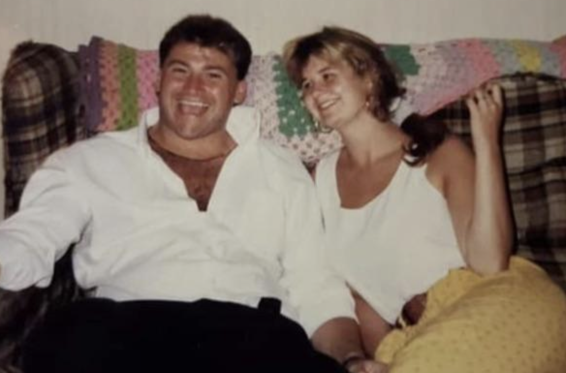 A man and a woman sitting together on a couch, smiling and looking toward the camera.