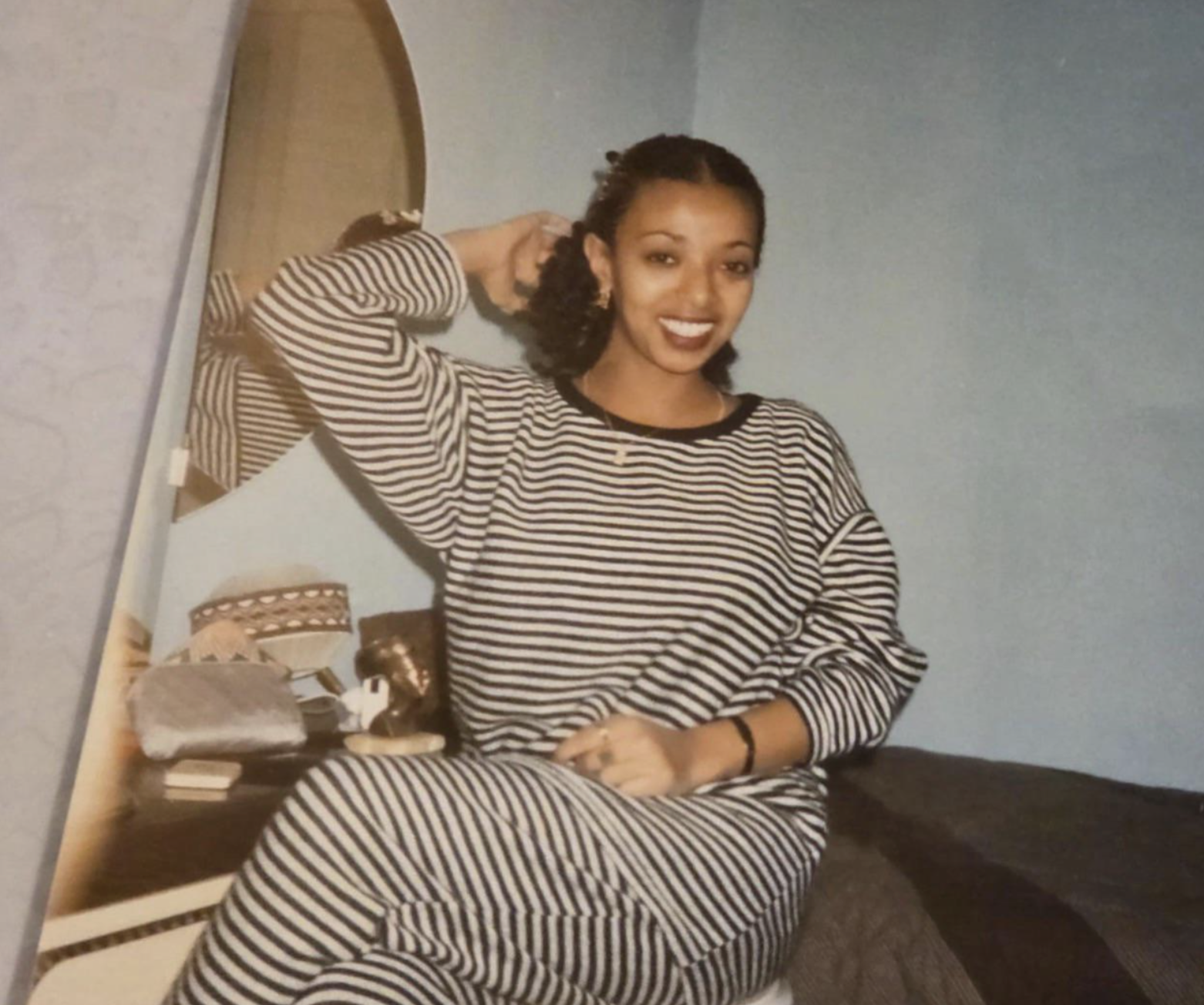 A woman smiling while wearing a long-sleeved, striped matching set, sitting in front of a mirror.