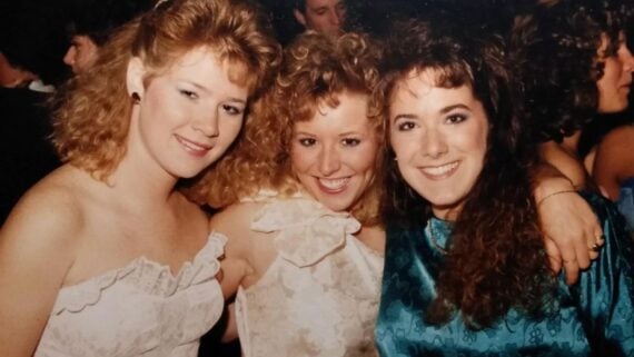 Three young women smiling together at an evening event.