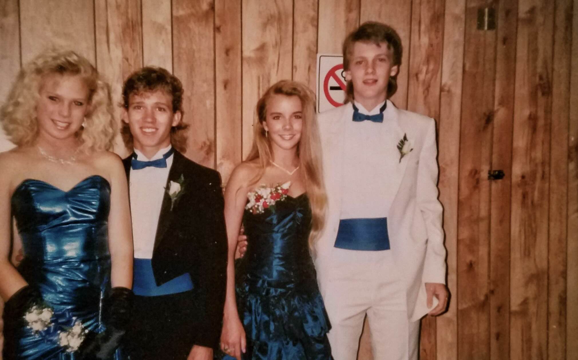 Two couples pose for a photo at a formal dance, wearing matching blue and white tuxedos and metallic blue gowns.
