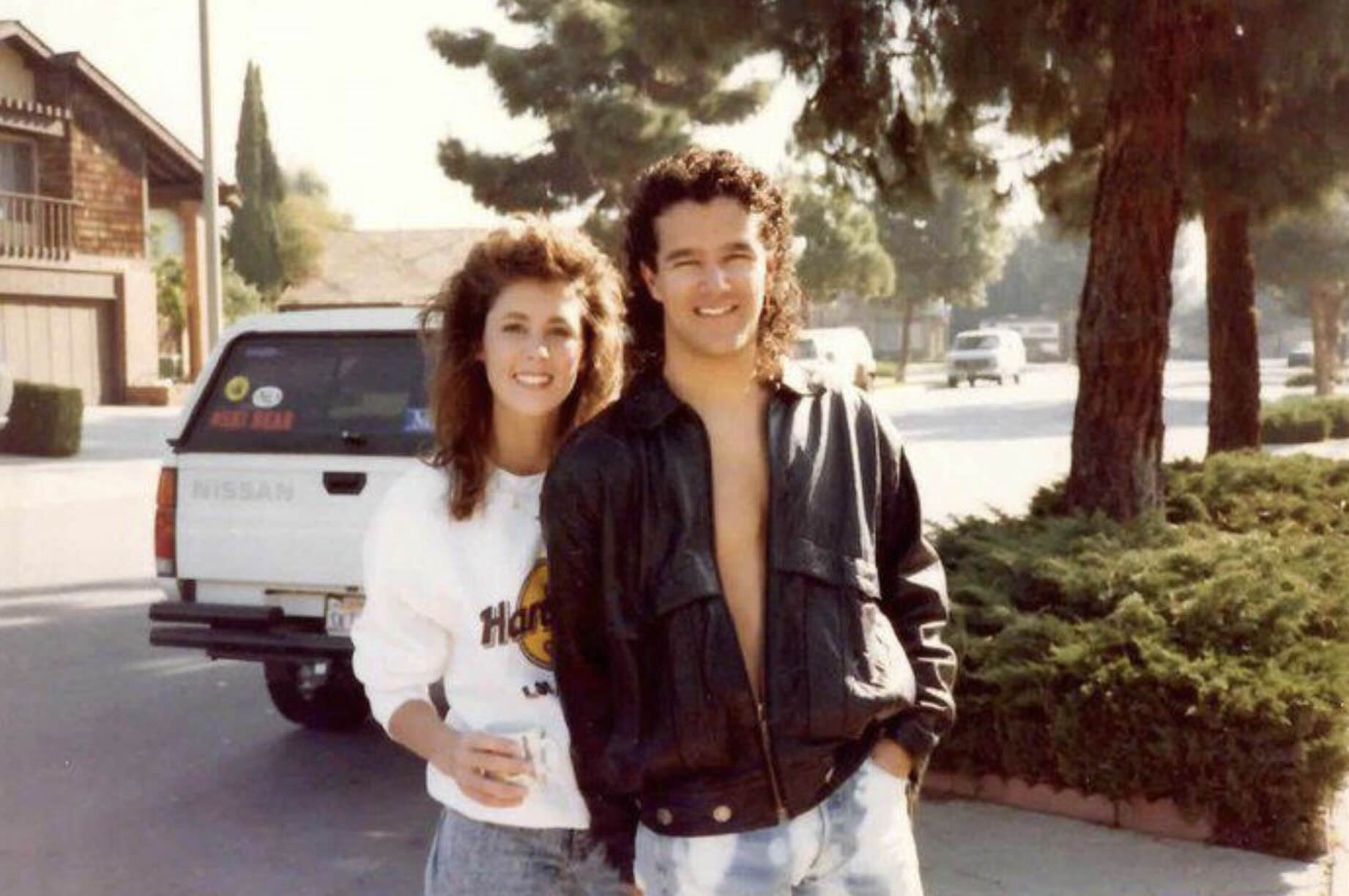 A man and woman posing for a photo outdoors in front of a parked Nissan vehicle.