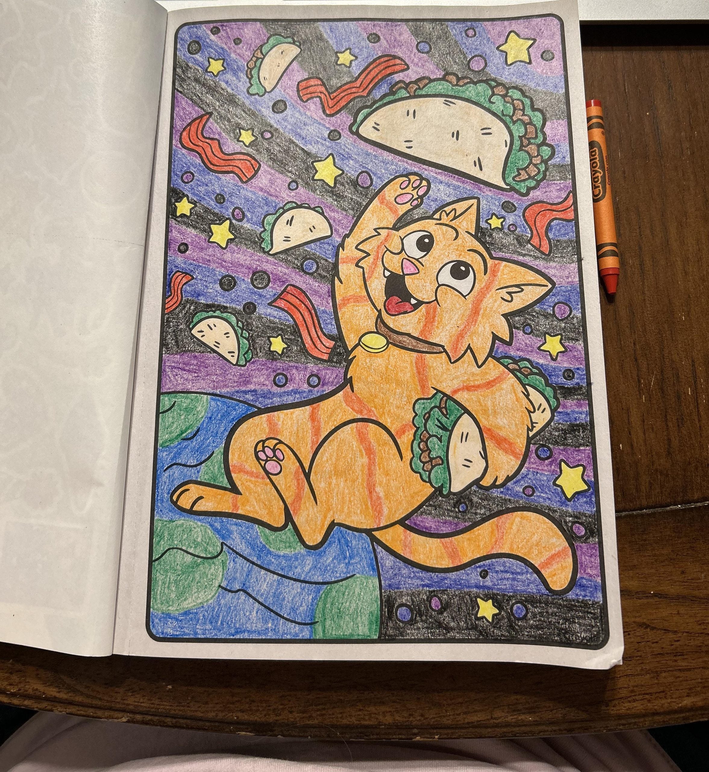 A colored-in page from a coloring book showing an orange cat floating in space surrounded by tacos, bacon strips, and stars above the Earth.