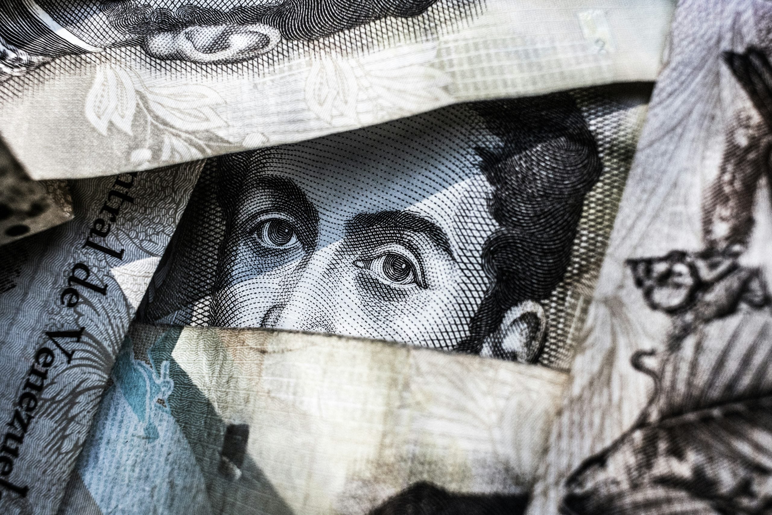 Close-up of a portrait on a Venezuelan bolívar banknote peeking through layers of currency.