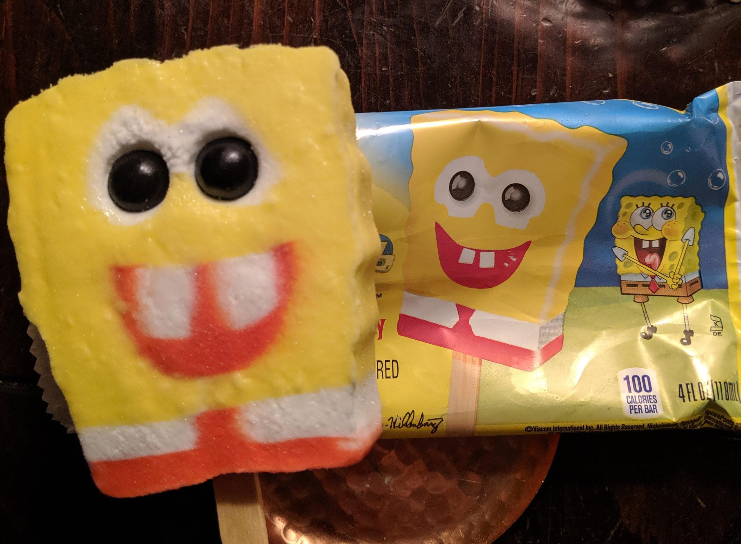 A SpongeBob SquarePants popsicle next to its branded yellow wrapper.