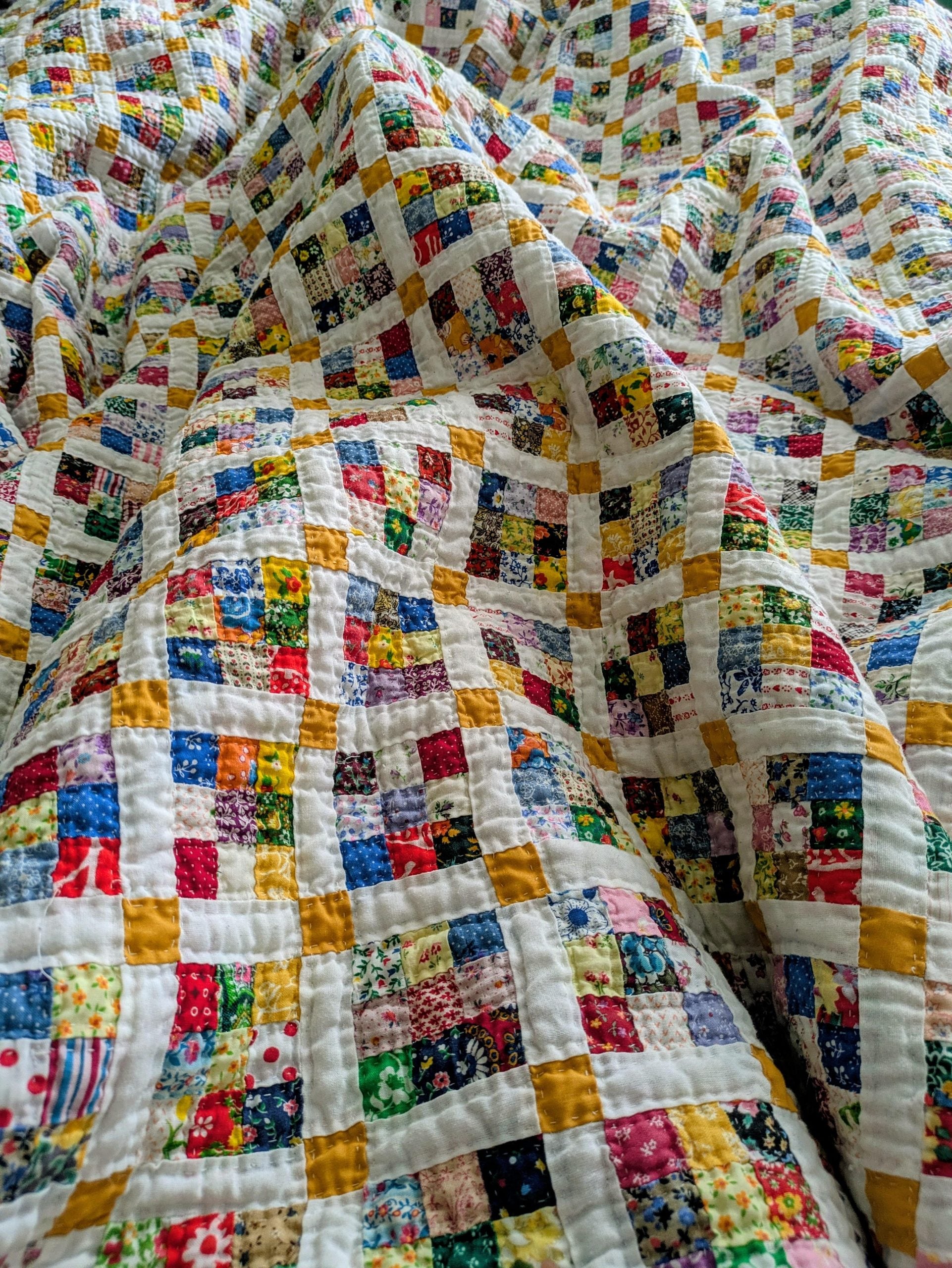 A colorful patchwork quilt made of tiny multicolored fabric squares separated by thin white and yellow grid lines.