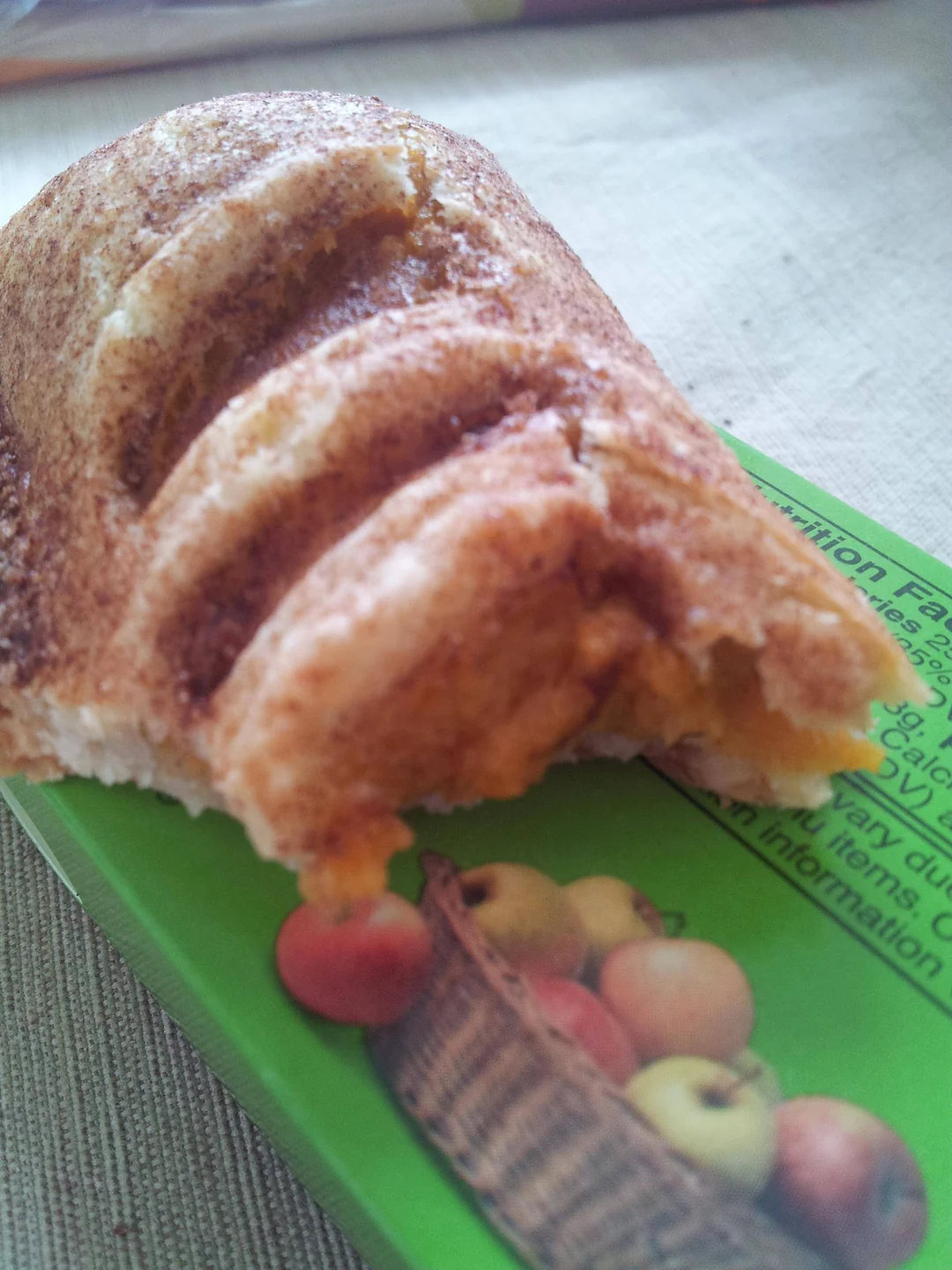 A bitten cinnamon pastry resting on top of a green apple-flavored nutrition bar box.