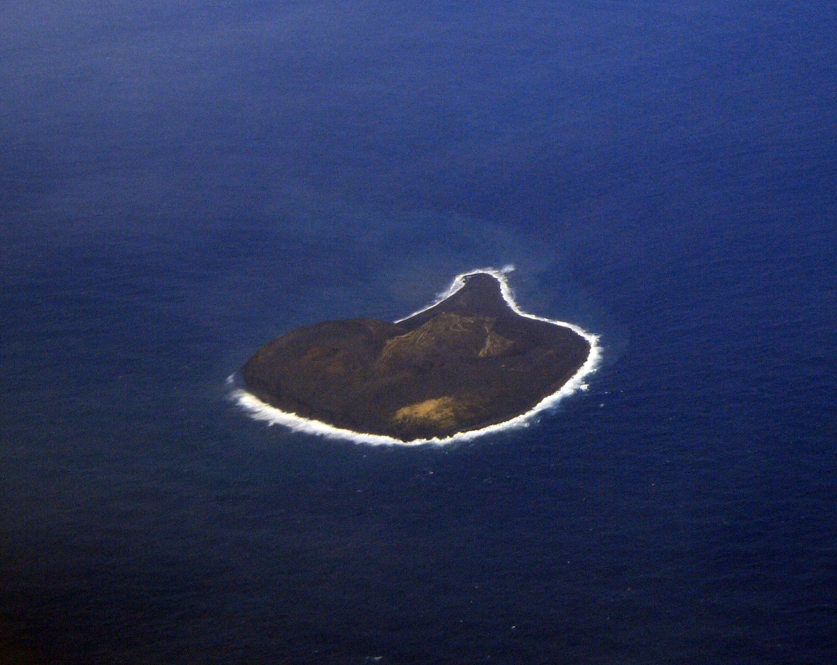 Aerial view of a heart-shaped volcanic island surrounded by deep blue ocean.